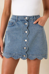 Close view of medium wash denim skirt highlighting scalloped button-front accents.