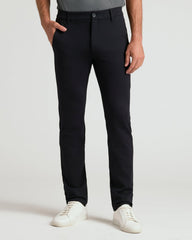 A person wearing slim-fit black trousers, paired with a gray top and white sneakers, standing against a light gray studio background.