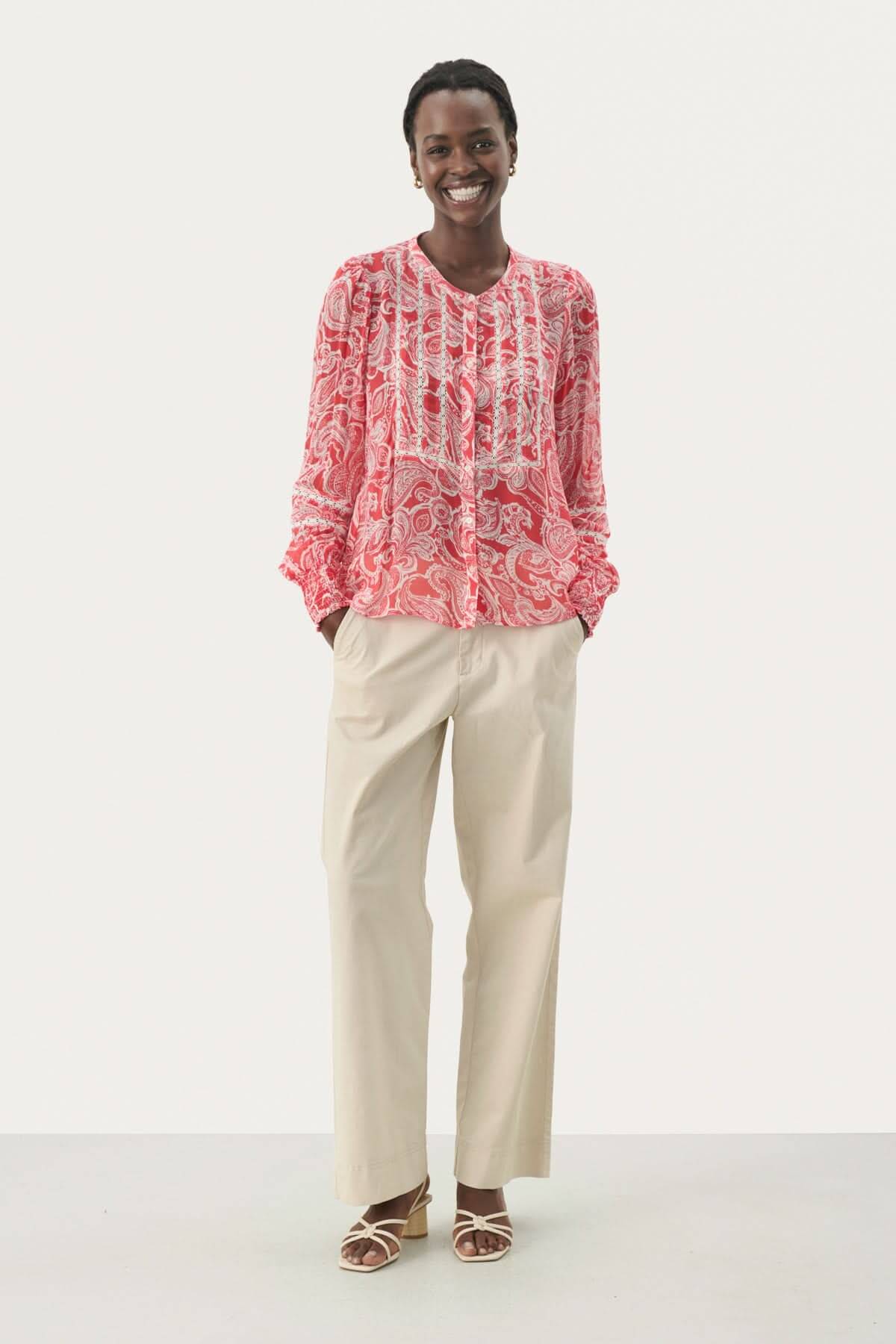 Blouse fluide Nesma à micro-motif fleuri, manches longues, portée avec un pantalon beige.