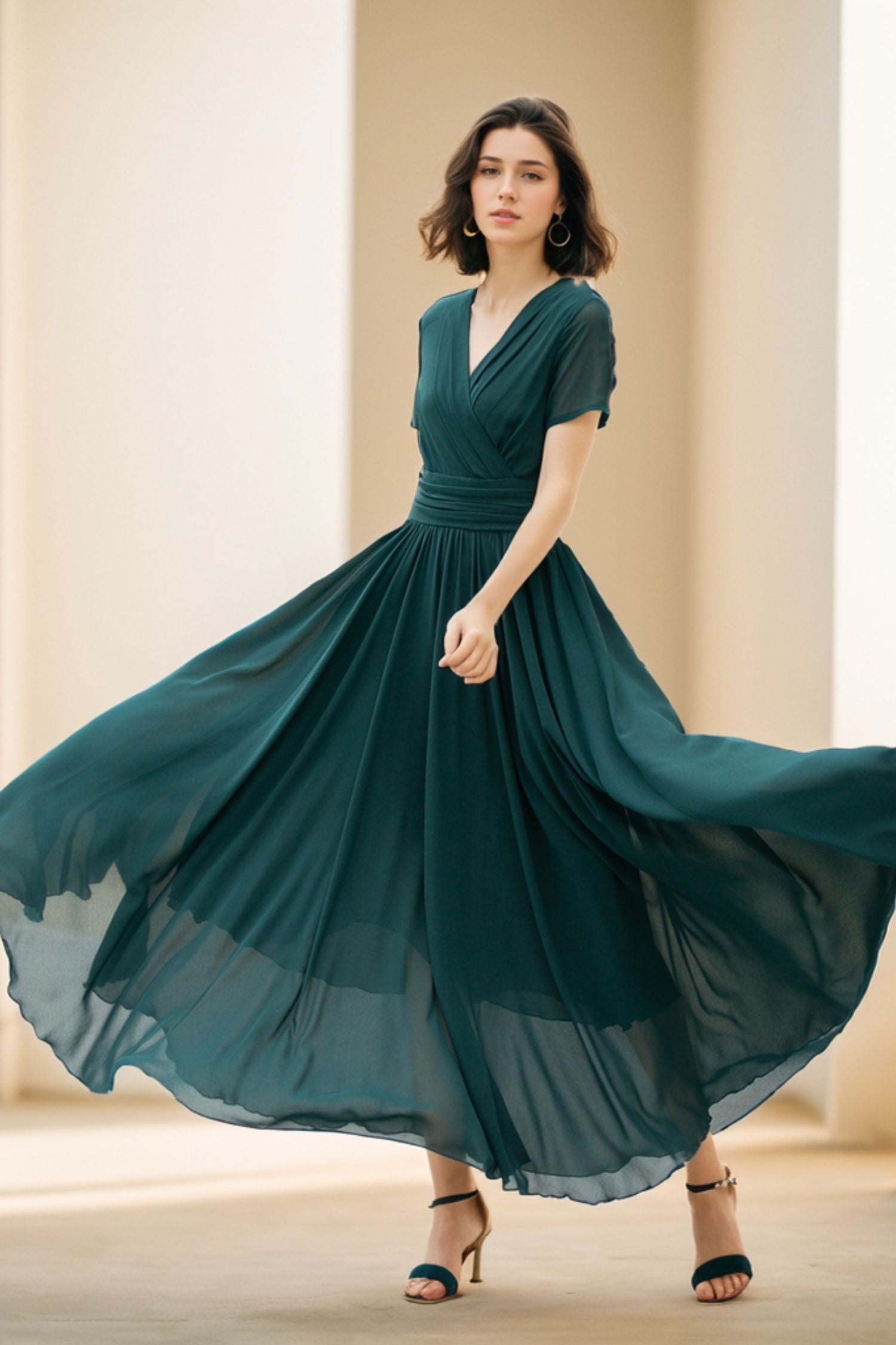 A woman in a flowing teal chiffon maxi dress with a V-neckline and short sleeves, dancing with her hands raised and flowing skirt.
